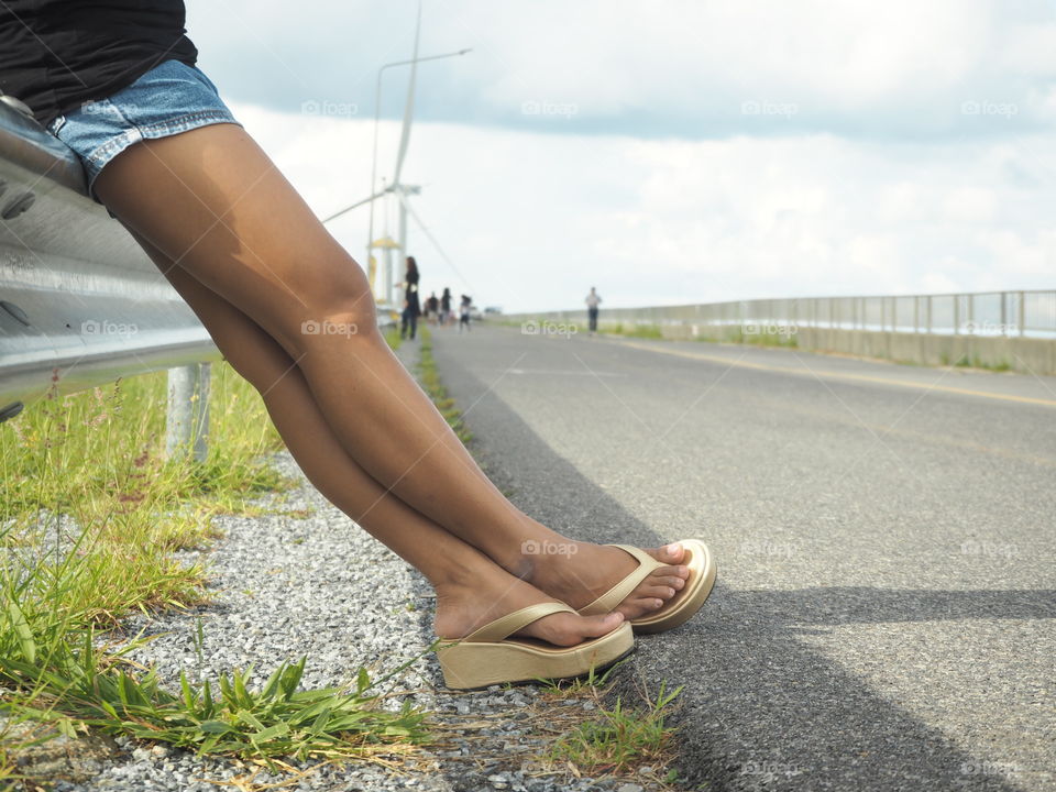 closeup leg of asia girl with road background blur,sky and dam