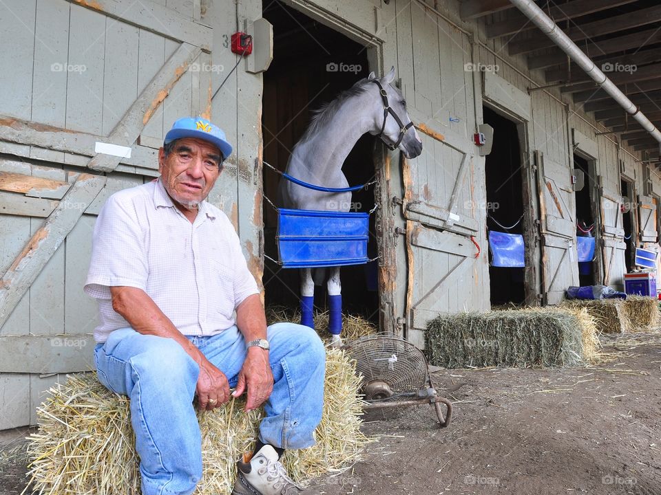 Saratoga Backstretch Worker. Behind the scenes on the backstretch of the oldest track in America "Saratoga" this worker is resting on a bale of hay.