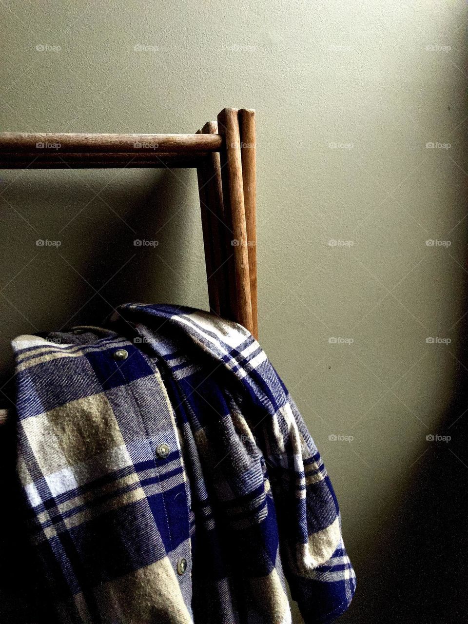 Plaid flannel shirt folded on wooden clothes rack in partial shadow, against a gray interior wall.
