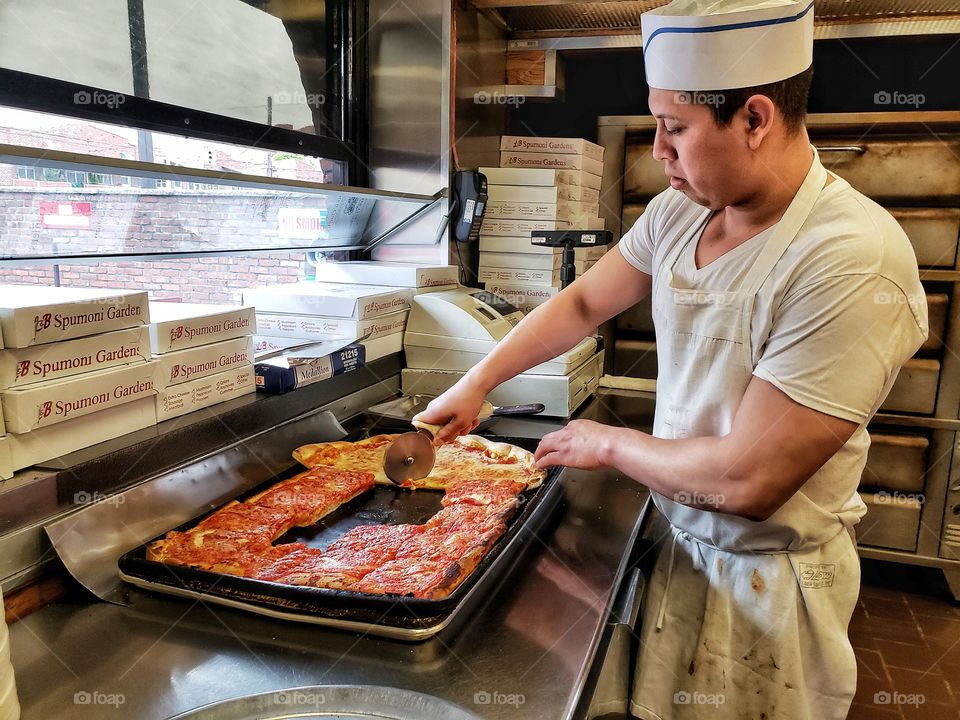 Chef cuts slices of Sicilian and Neapolitan pizza in a pizzeria