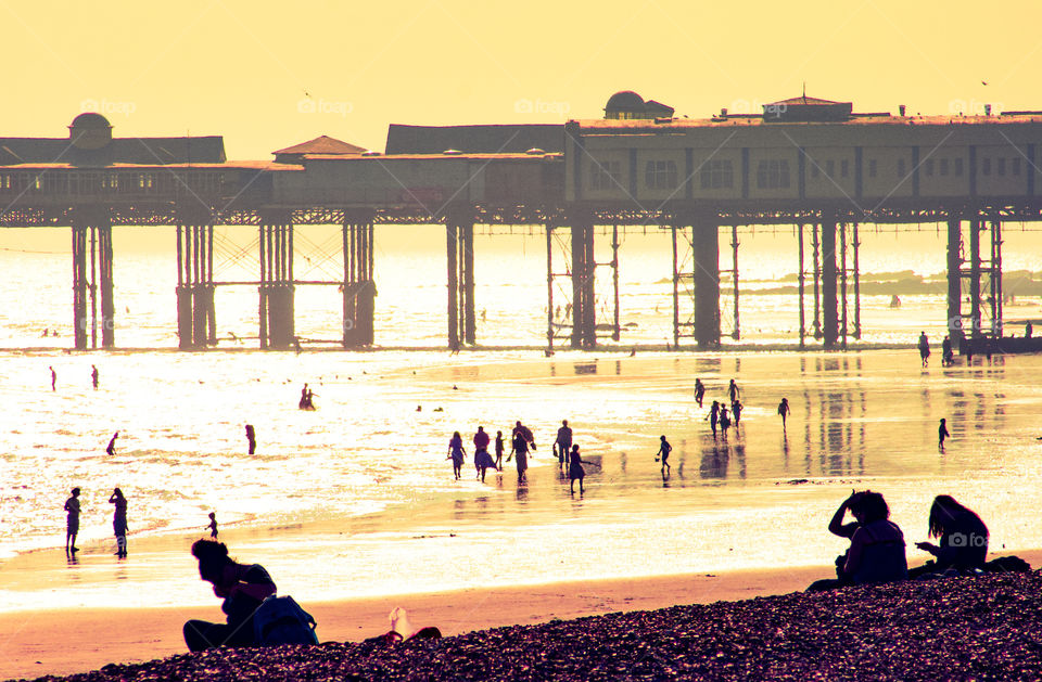 A hot sunny day on Hastings beach. The tide is out, the sun is low and silhouetting the pier and holiday makers on the beach