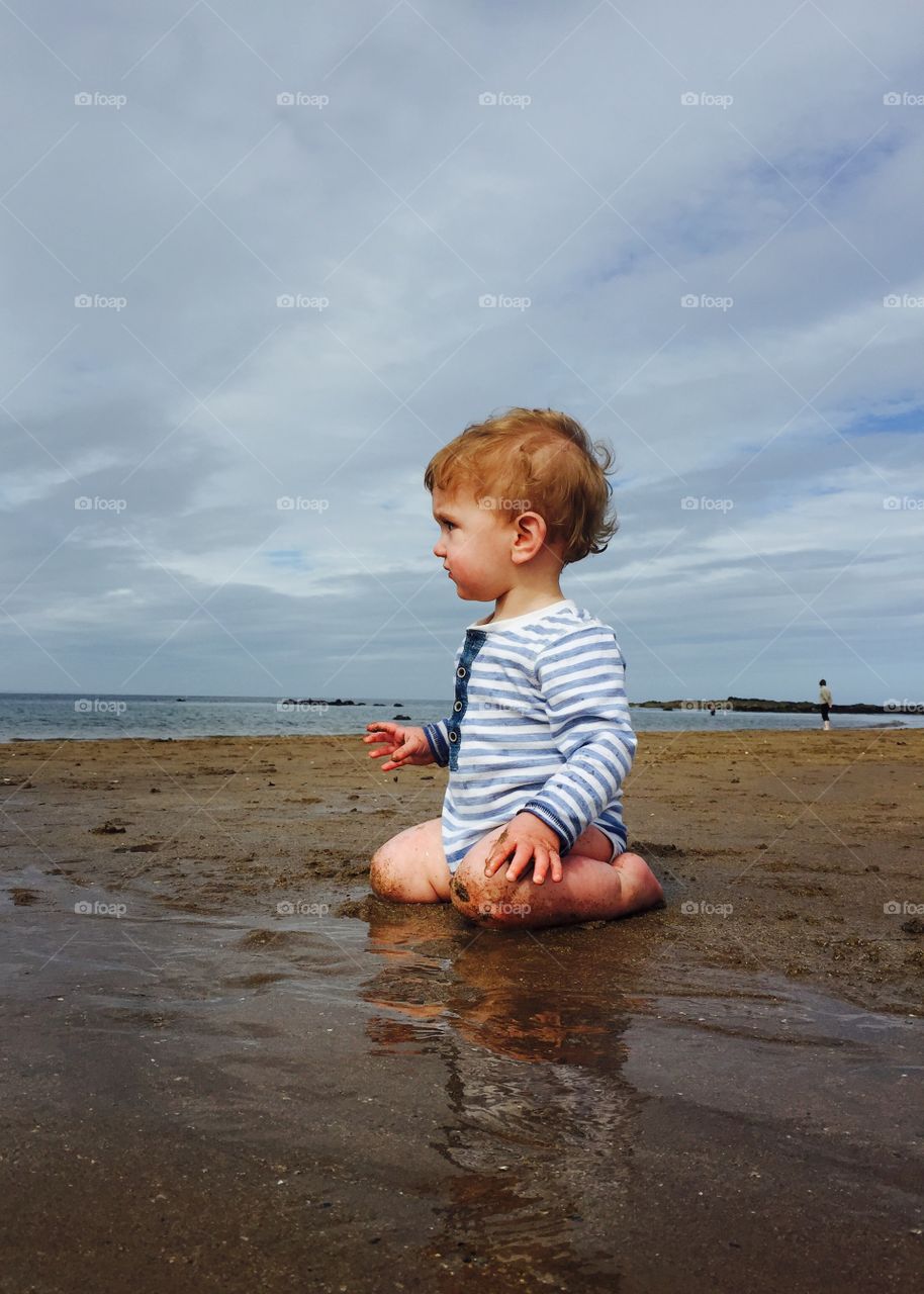 Cute boy sitting on sand at beach