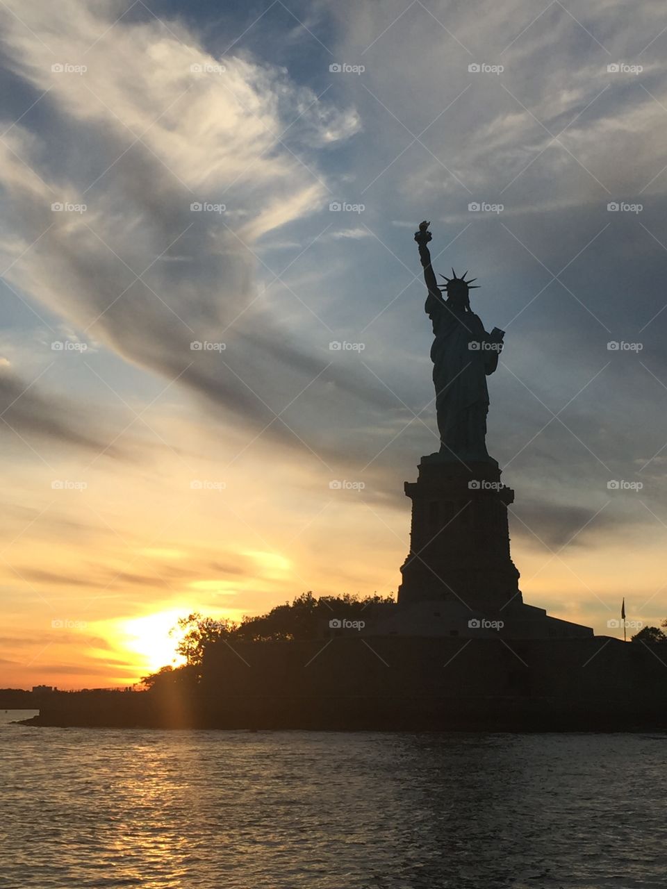 Silhouette of the Statue of Liberty at sunset with wispy clouds 