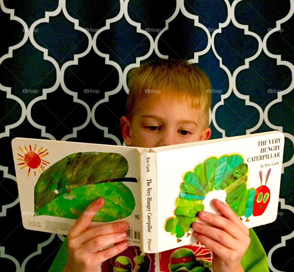 Little boy reading a popular children’s book by Eric Carle called The Very Hungry Caterpillar 