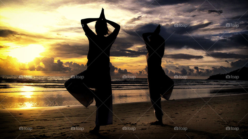 Yoga duo at sunset. Beautiful scenery of two girls doing yoga at the beach