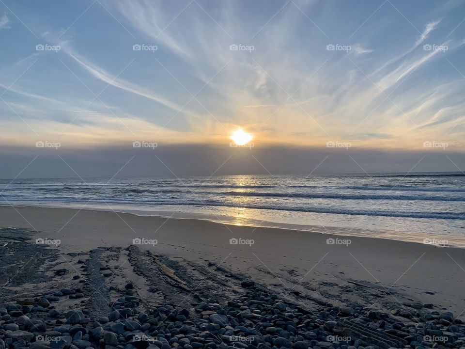 The setting sun dips below a cloud bank formed over the Atlantic Ocean at Praia Pedra do Ouro, Portugal 