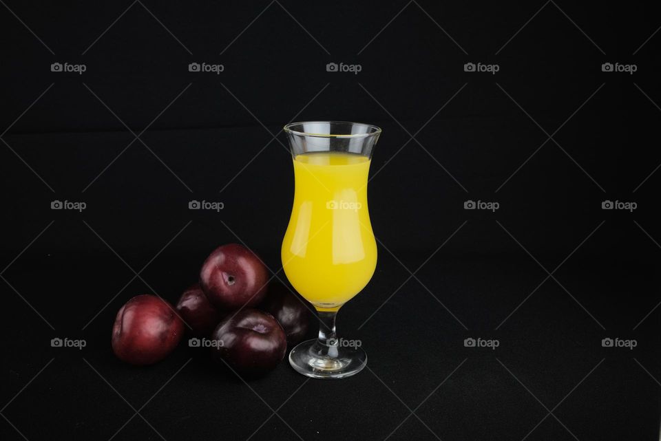 Red plums with a glass with natural juice on a black background