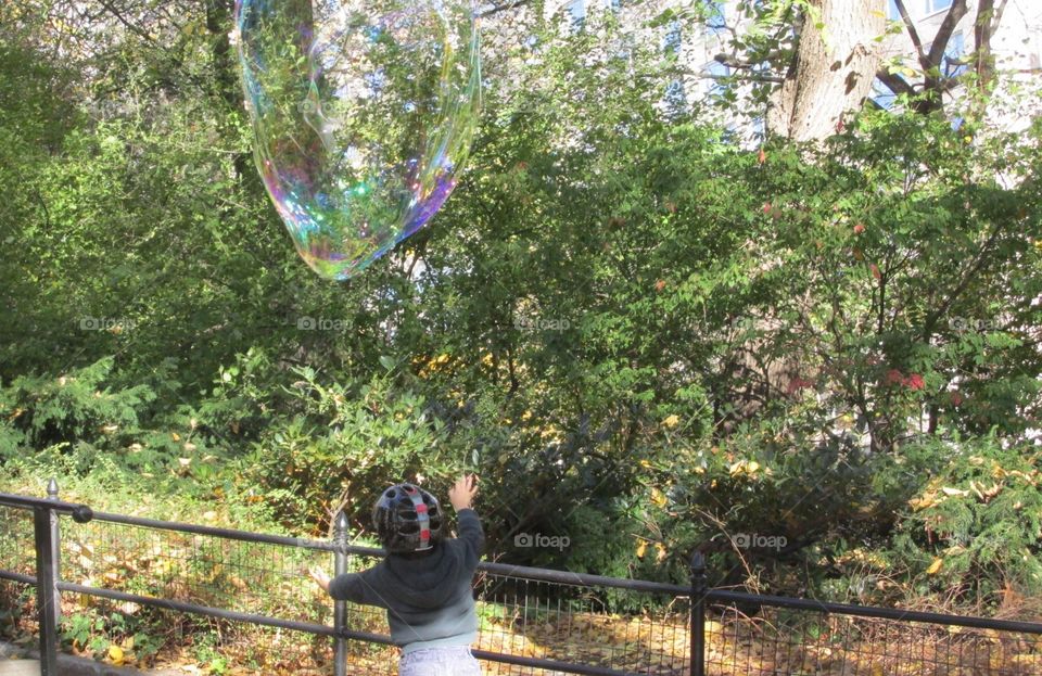 Young Child with Helmet Chasing a Giant Bubble in Central Park on a Sunny Autumn Day