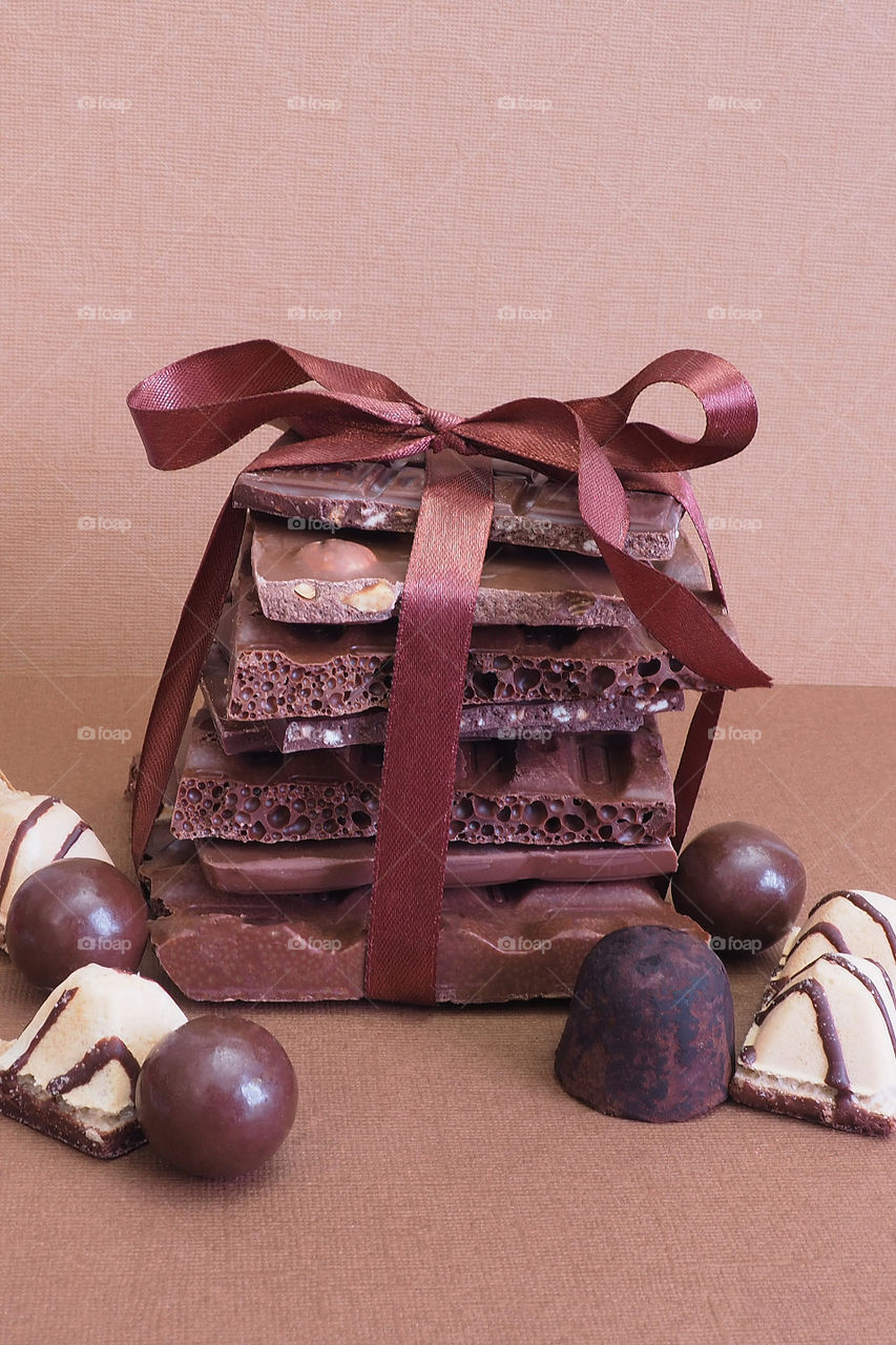a stack of broken chocolate tied with a brown satin ribbon and chocolates on a brown background