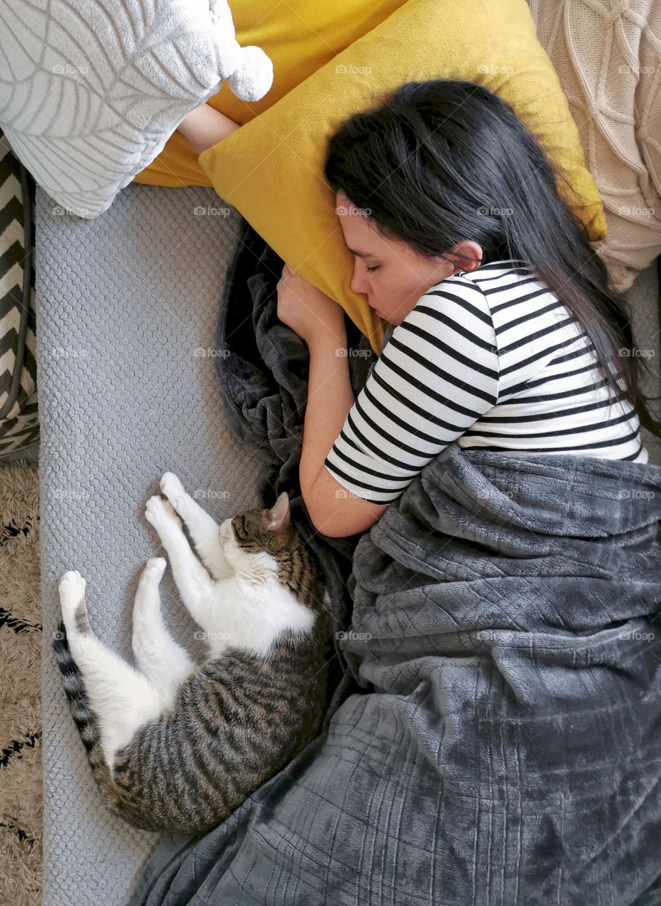 Overhead photo of young woman and her cat taking a nap on couch