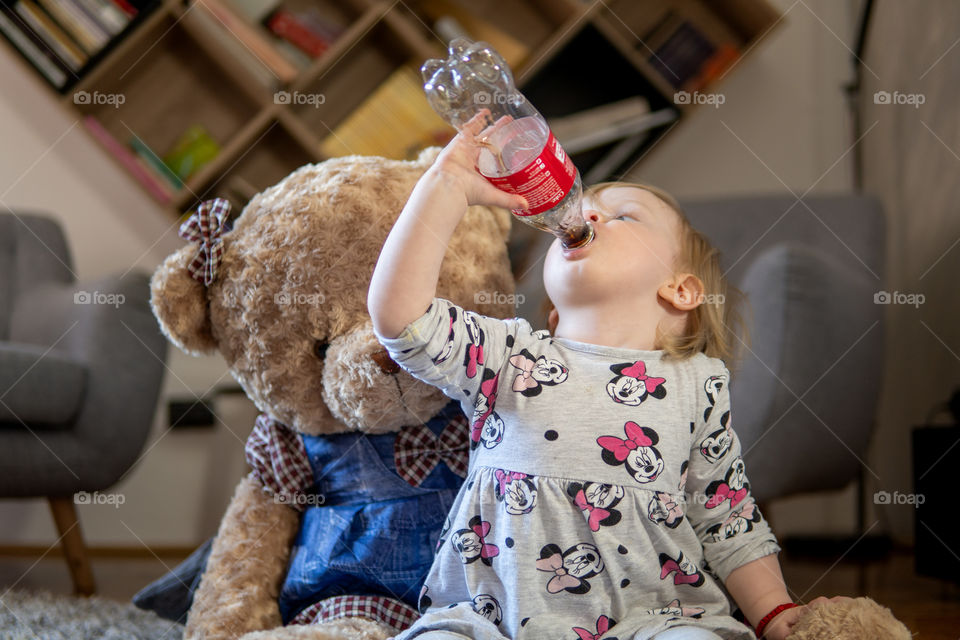 Girl drinking last drops of coca cola with teddy bear