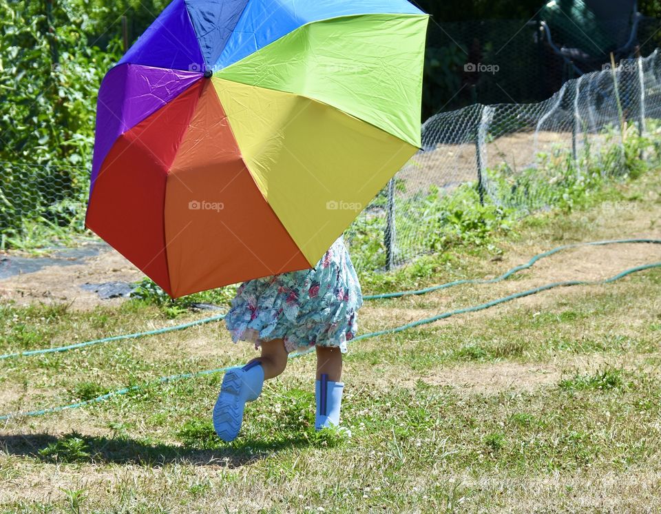 Colorful umbrella held by a little girl in a blue flowery dress running