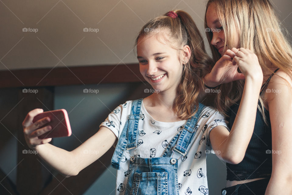 Young women taking selfie, using smartphone camera. Girls making faces, enjoying taking funny pictures together