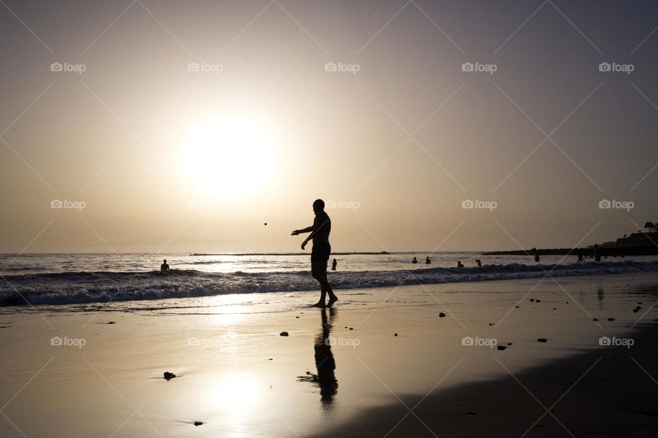 person throwing a stone into the sea at sunset