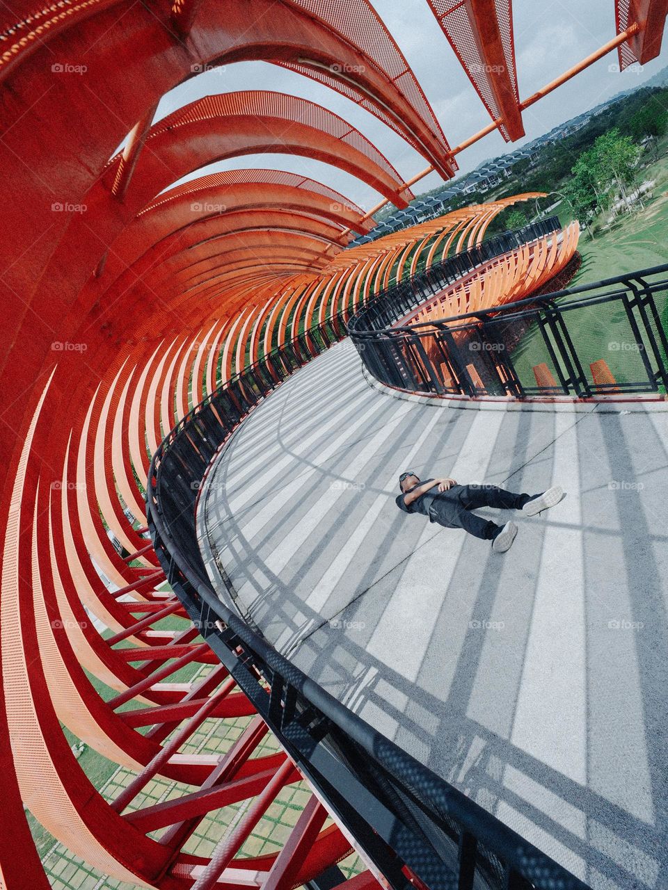 A boy lying down on a dynamic designed curved pedestrian bridge