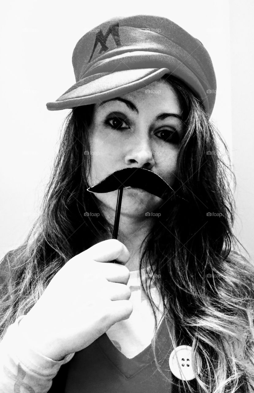 woman holding a mustache on a stick up to her face dressed as Mario