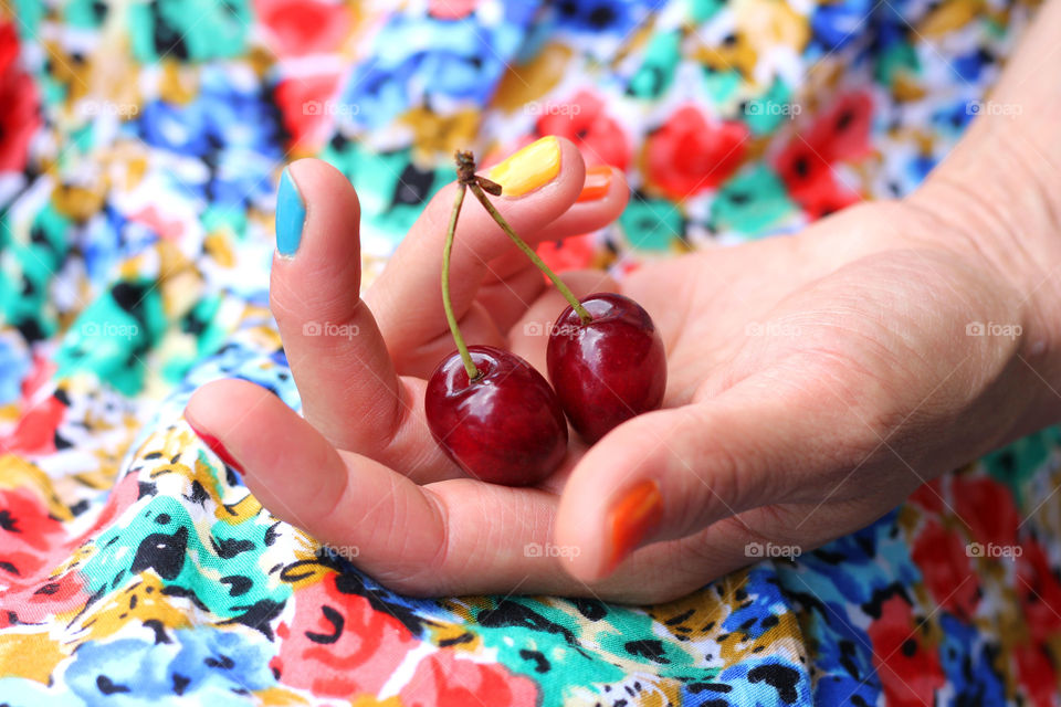 A hand with colorful nail polish holding cherries on colorful dress background