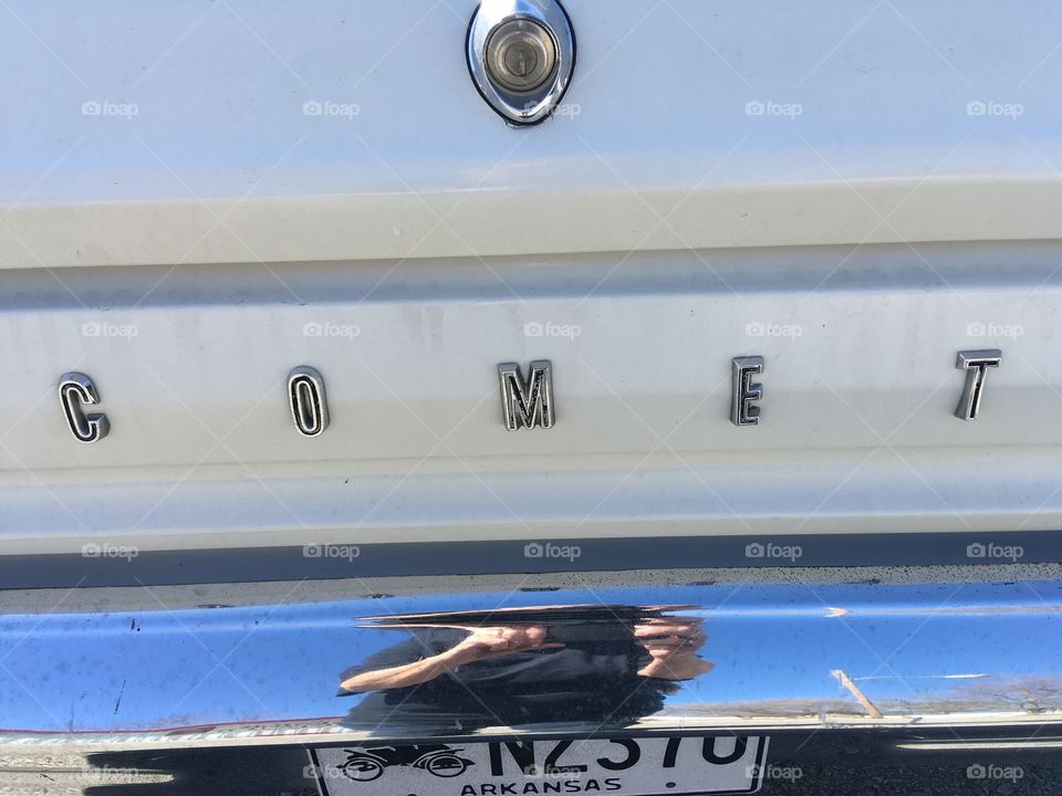 Trunk of a 1966 yellow comet showing the chrome bumper. Very shiny and clean. Bumper shows my reflection.