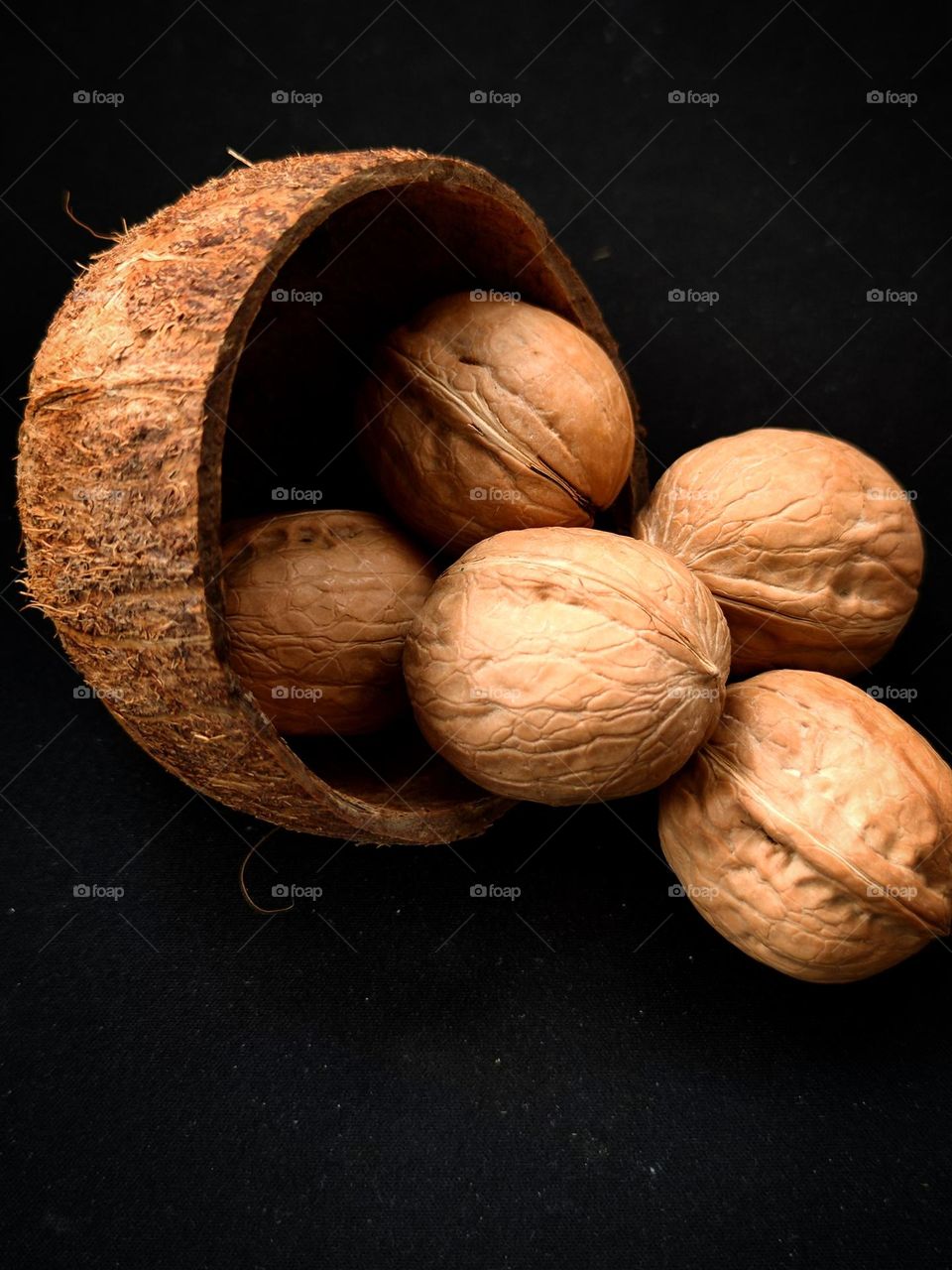 Fruits of walnuts and half of a coconut on a black background