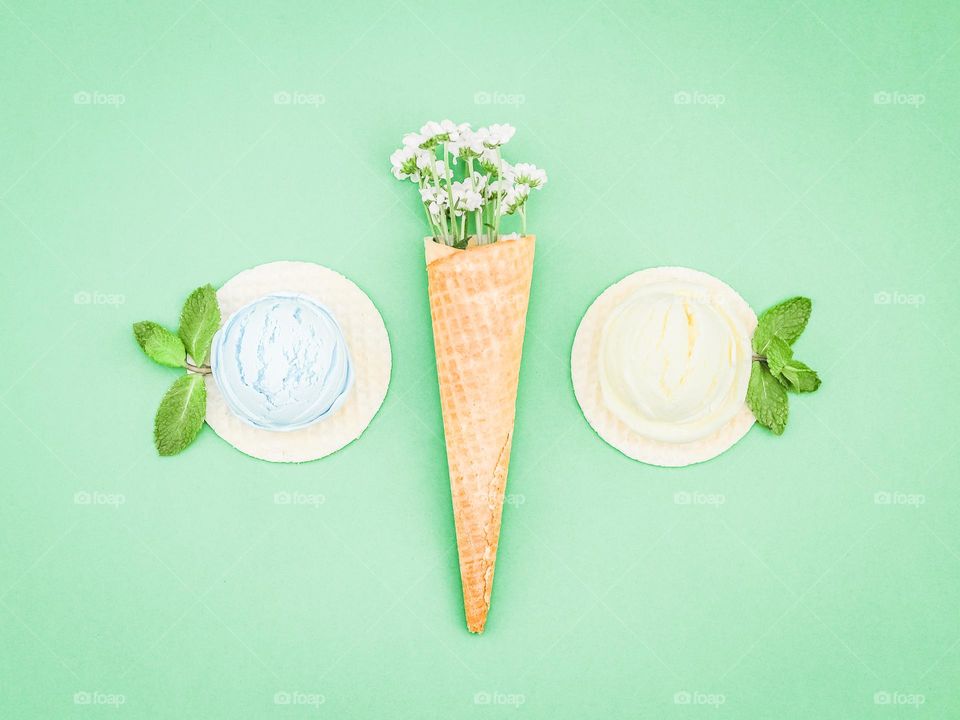 Two balls of berry ice cream on round wafers and one wafer cone with flowers lie in the center on a green background, flatley close-ups. Concept summer treat, summer food, natural ice cream.