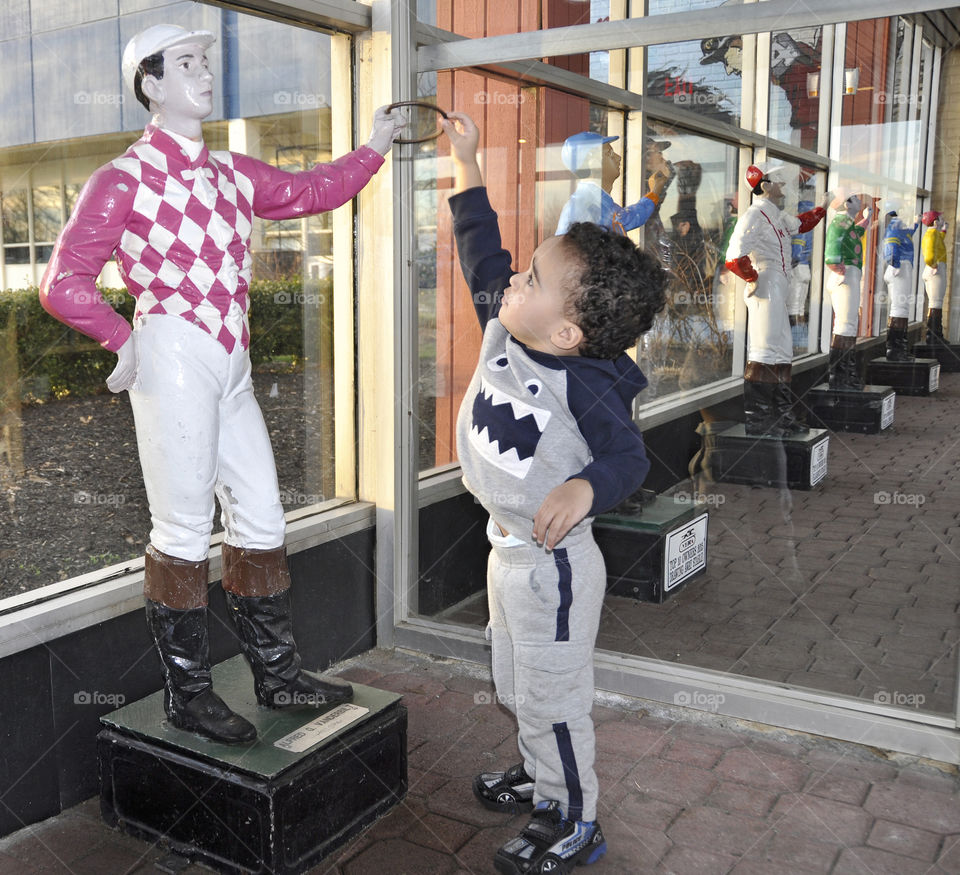To Little to be the Man!
A young boy reaches high to touch the hand of a pink and white diamond painted silks of the famous Vanderbilt colors at Aqueduct.

zazzle.com/Fleetphoto