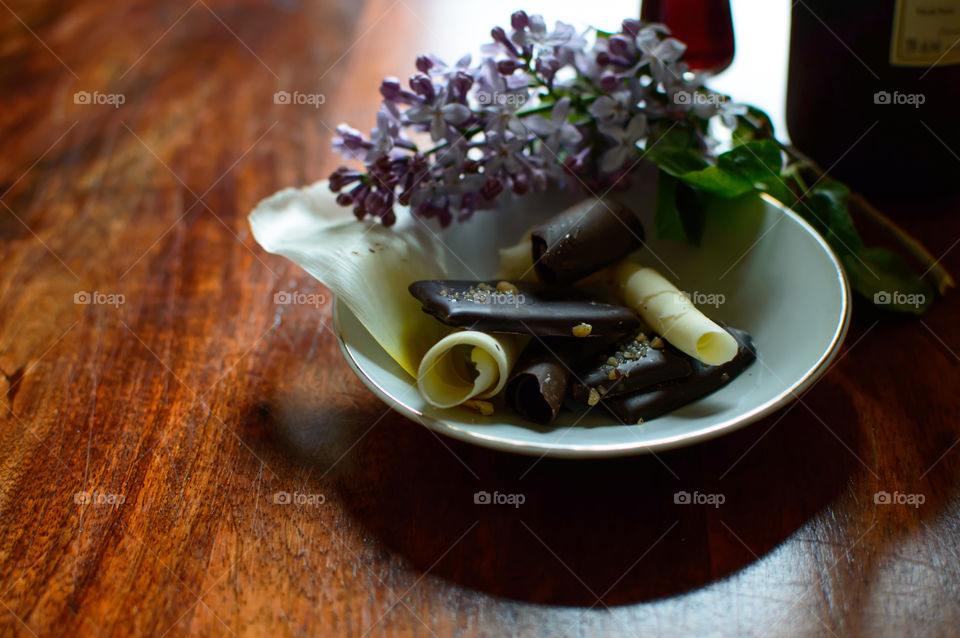 Gourmet chocolate pieces on plate with lilac flowers and port wine epicure dark and white chocolate decadent treat photography with room for copy