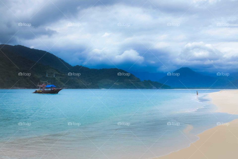Beautiful Shot a Ilha do Prumirim, Island at Ubatuba. We see a Woman wanting a Boat at the shore, beautiful blue shot.