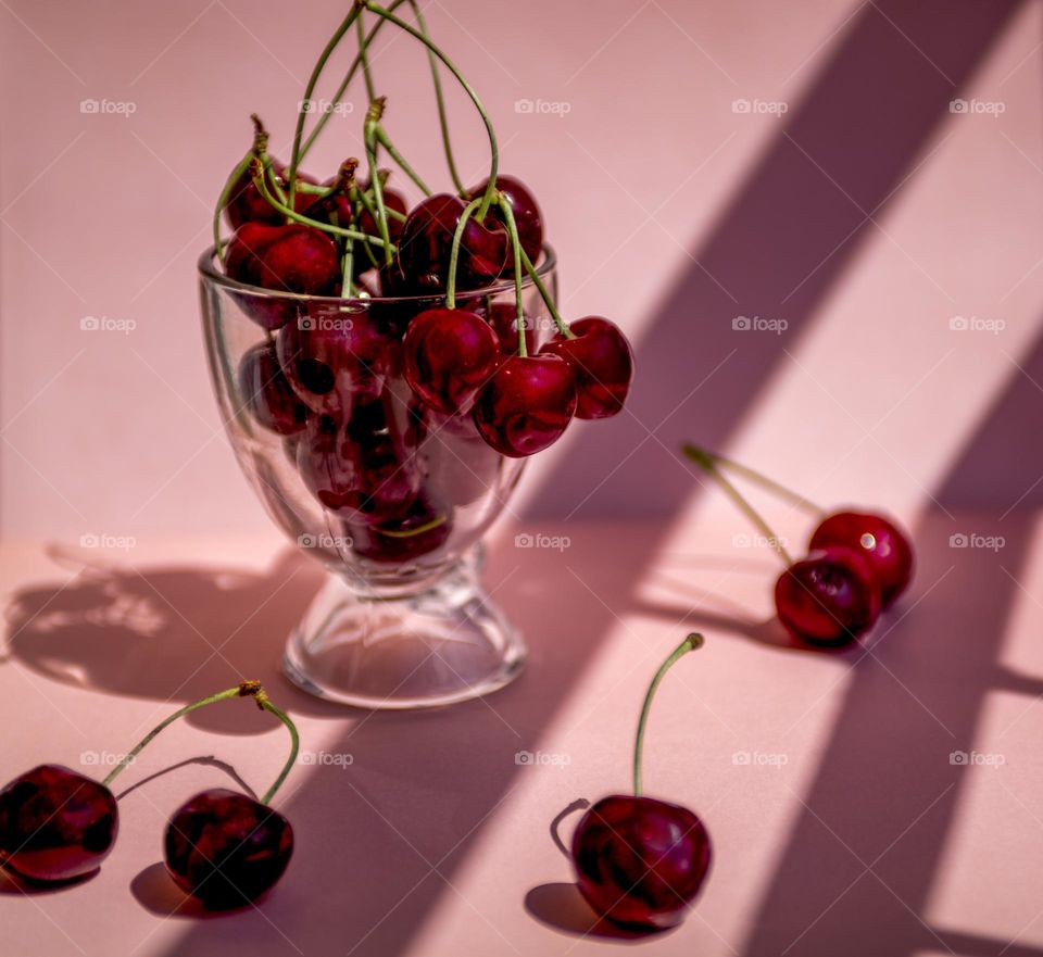 Ripe cherries in a glass on a pink background
