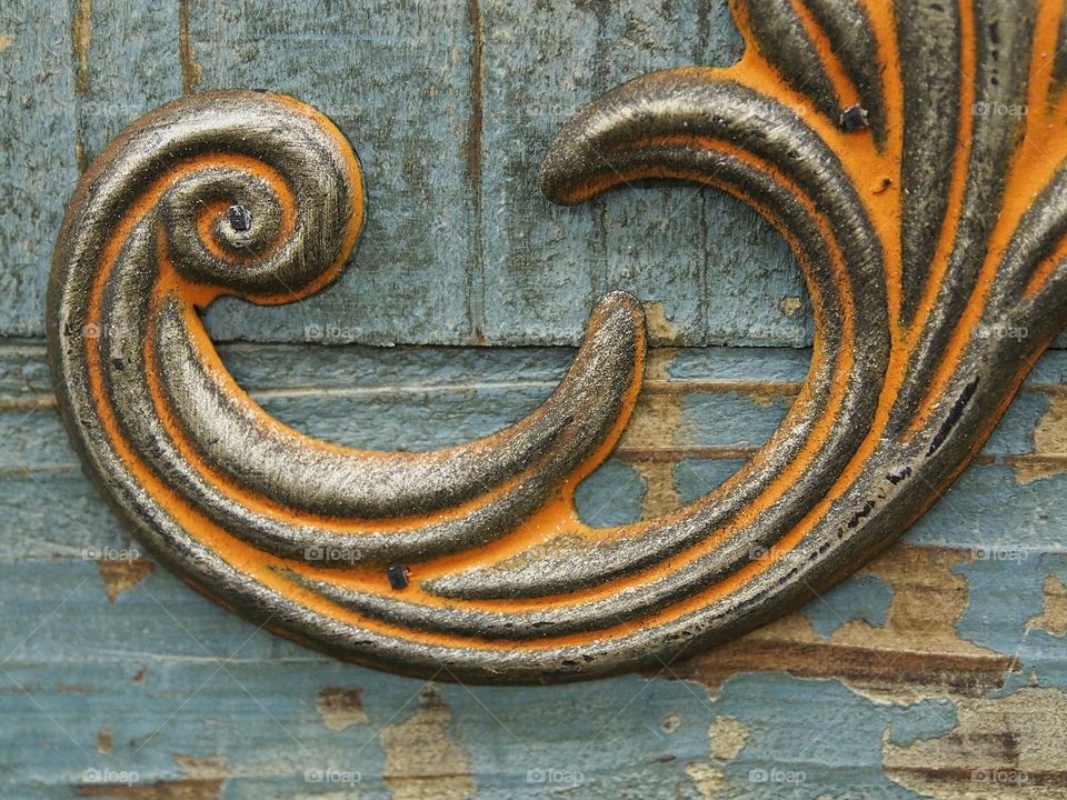 An ornamental piece of brass with an aged and rusted look attached to distressed blue piece of wood. 
