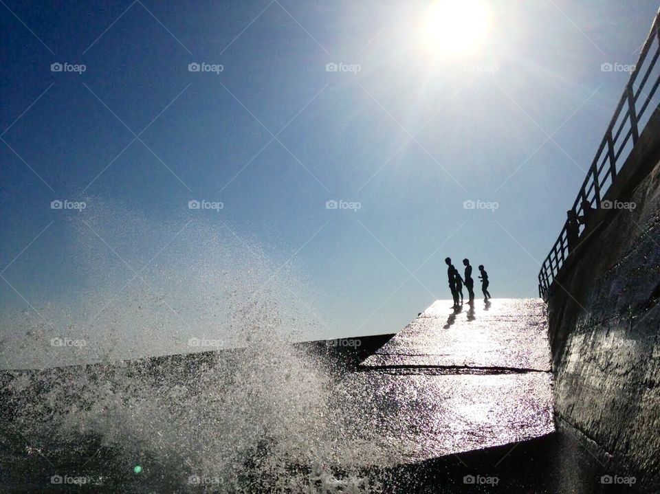 Silhouettes standing above the high waves and water splashes 