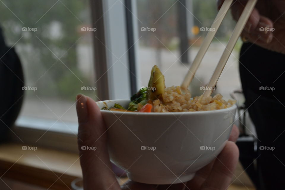 Woman's hand holding bowl of Asian food while using chopsticks 