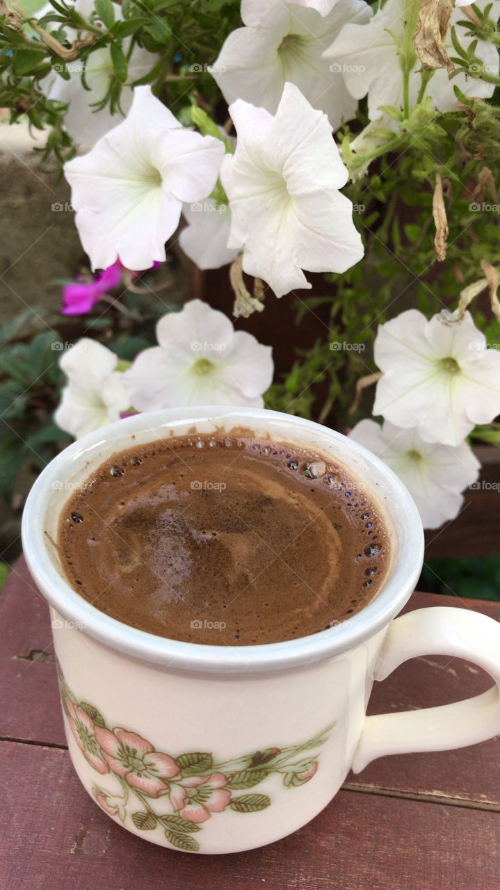 Lovely porcelain cup of coffee with black coffee in it, in the beautiful morning, surrounded by petunia flowers.
