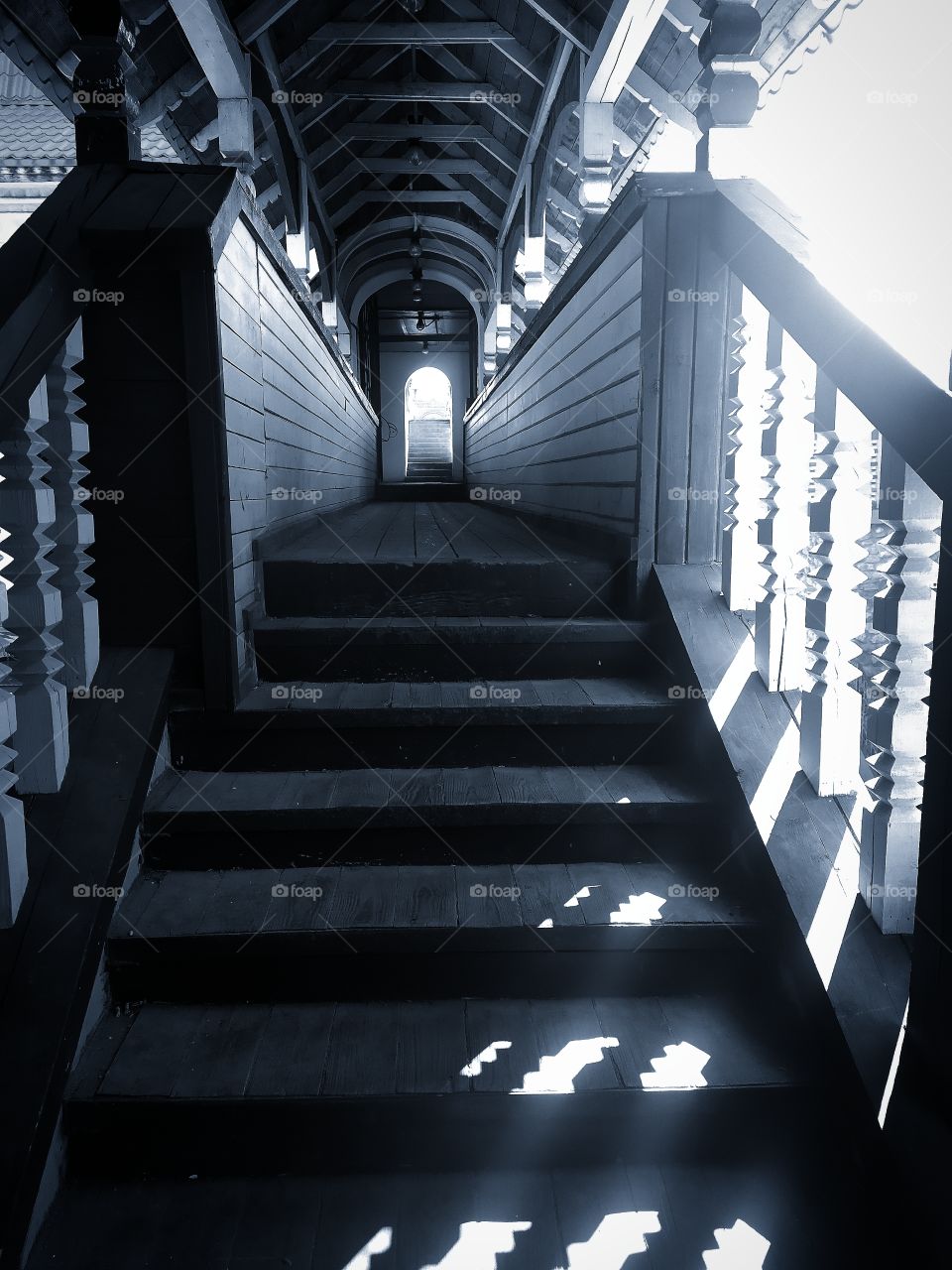 A wooden staircase that leads to a wooden bridge.  Sunlight shines through the railing