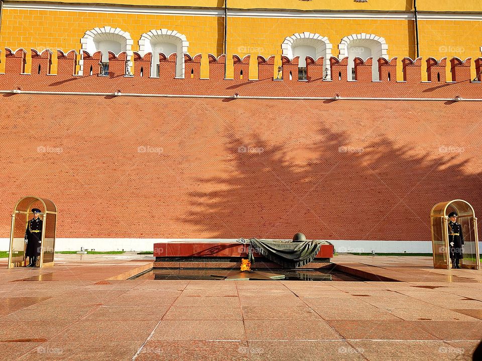Moscow.  Alexander Garden.  Memorial "Tomb of the Unknown Soldier".  Eternal flame.  Fire blazes from the five-pointed star.  Kremlin wall in the background.  On the sides of the memorial are cabins.  There is a guard soldier in each cabin.