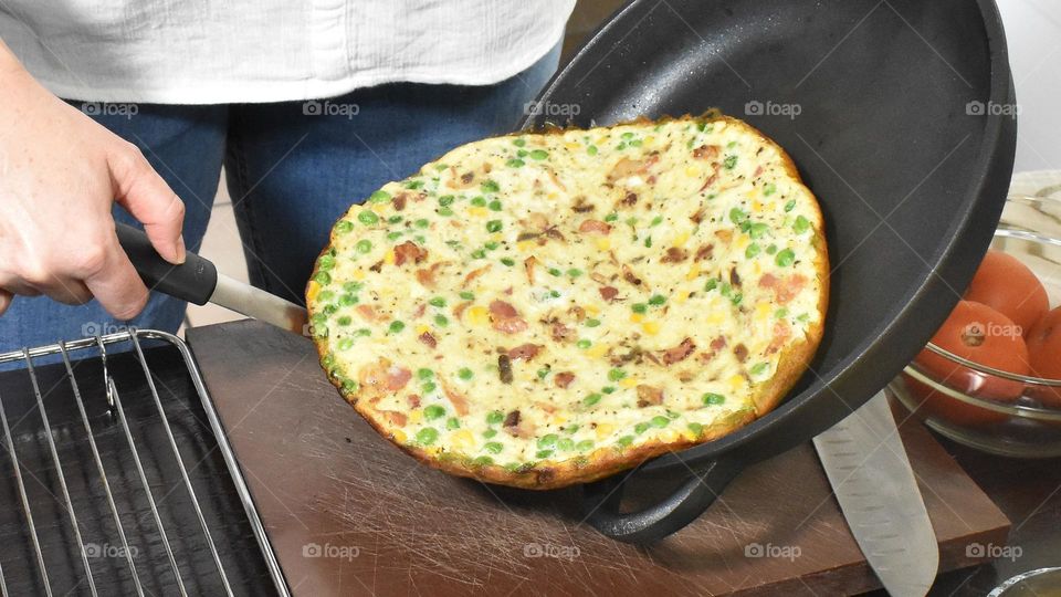 Homecooking cooking Frittata at home and adding and mixing ingredients and removing the Frittata from the pan for cutting and serving on a white plate with tomatoes. Healthy home cooking in kitchen. Breakfast and lunch food preparation.