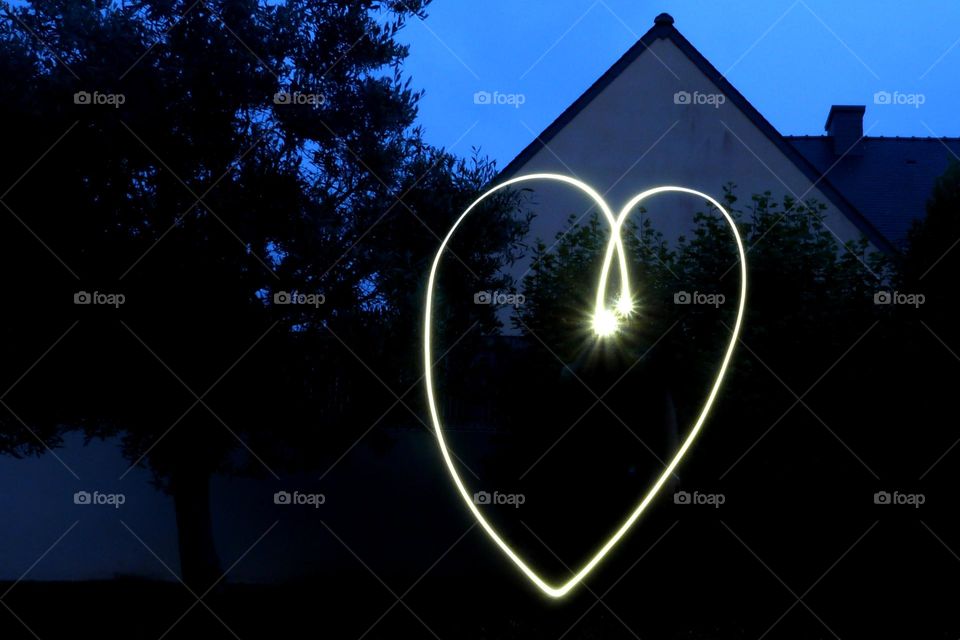 Light painting. A heart drawn with the long exposure technique in my garden at dusk. We can also distinguish the neighboring house and a tree.