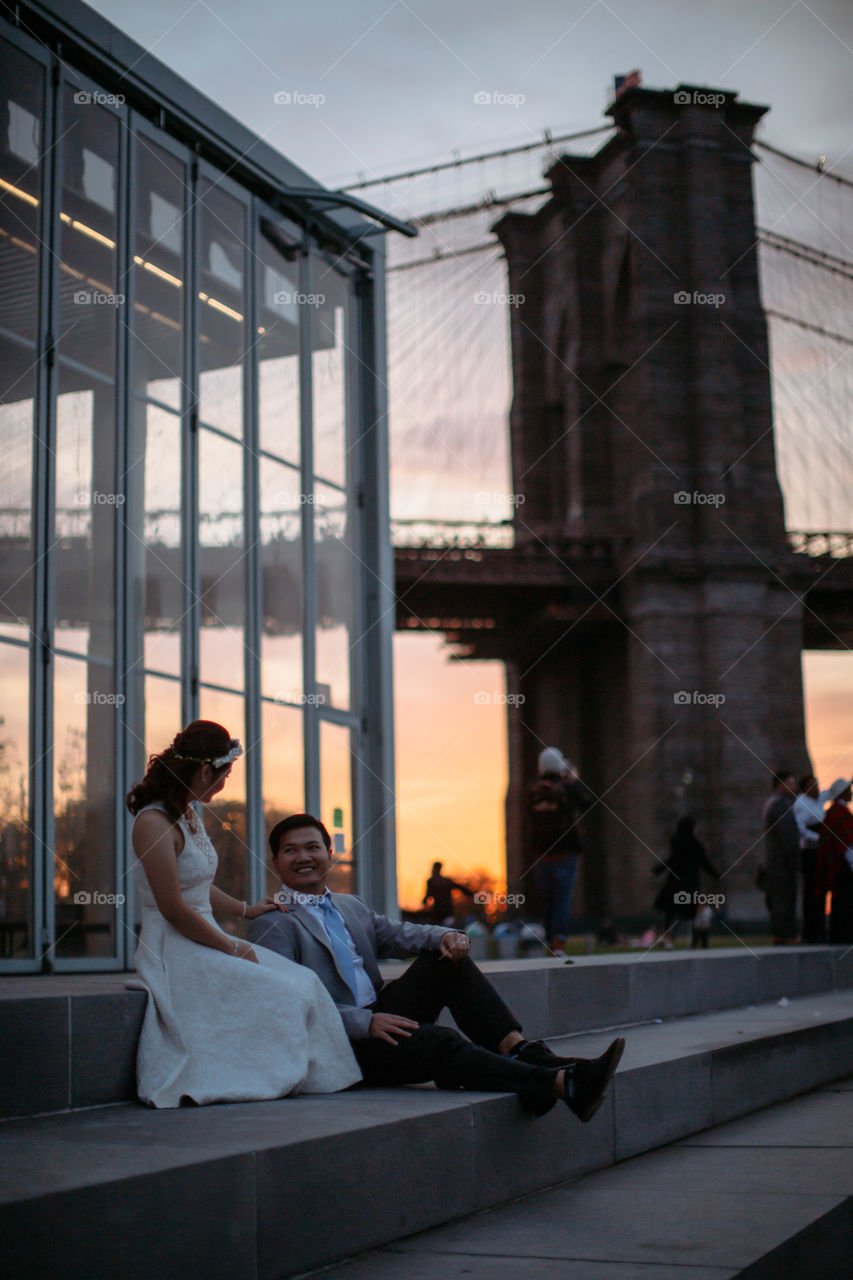 Happy couple sitting in front of bridge at dusk
