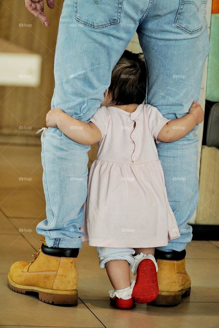 a two old baby who is learning to walk holding on to his father's knee