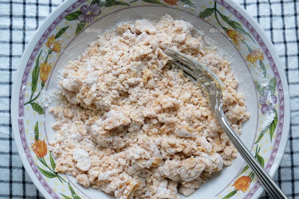 Preparing dough for American peanut butter cookies in the bowl with floral ornament with fork standing on the checkered napkin