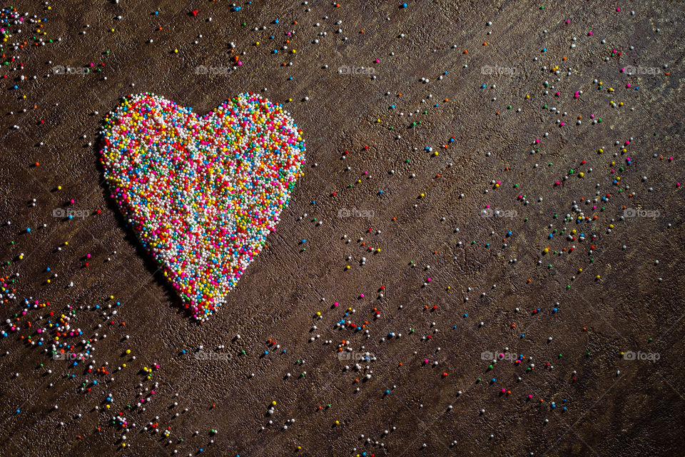 Heart shaped with ice cream and cake sprinkles using different colors. Dark textured background. Flat lay of heart.