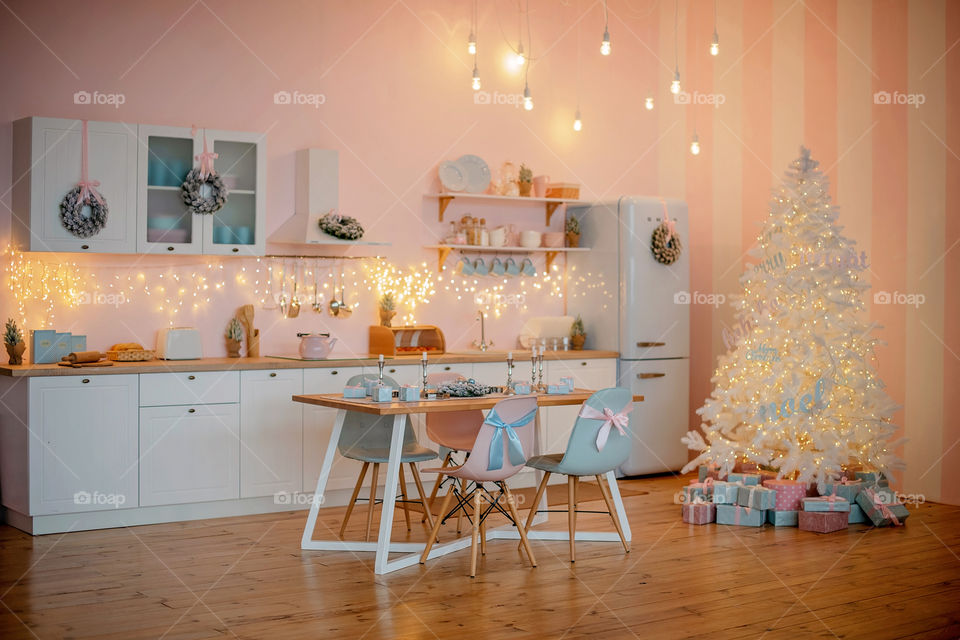 Festive winter cozy kitchen interior with garlands, decorations and gifts.  Christmas dinner at the decorated table.