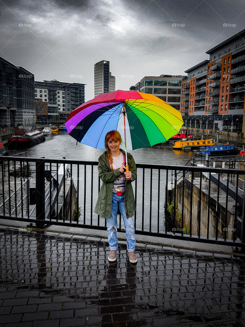Pretty girl standing near a canal in a city, in the rain holding colourful umbrella.