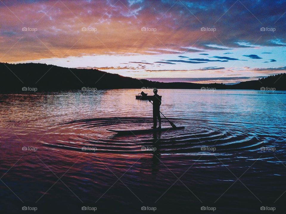A young man longboarding on a lake at sunset