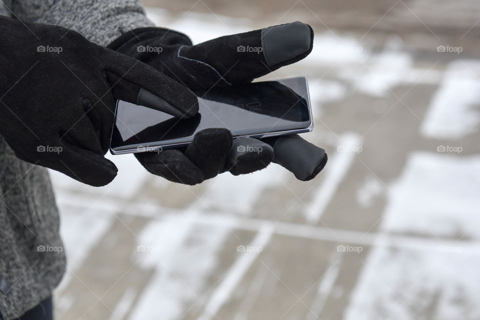 Person using a smartphone with tech gloves outdoors in the winter