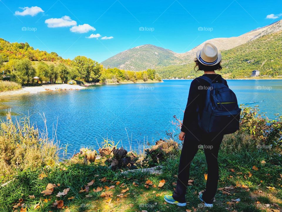 woman hiker from behind with hat, looks at Lake Scanno in Abruzzo