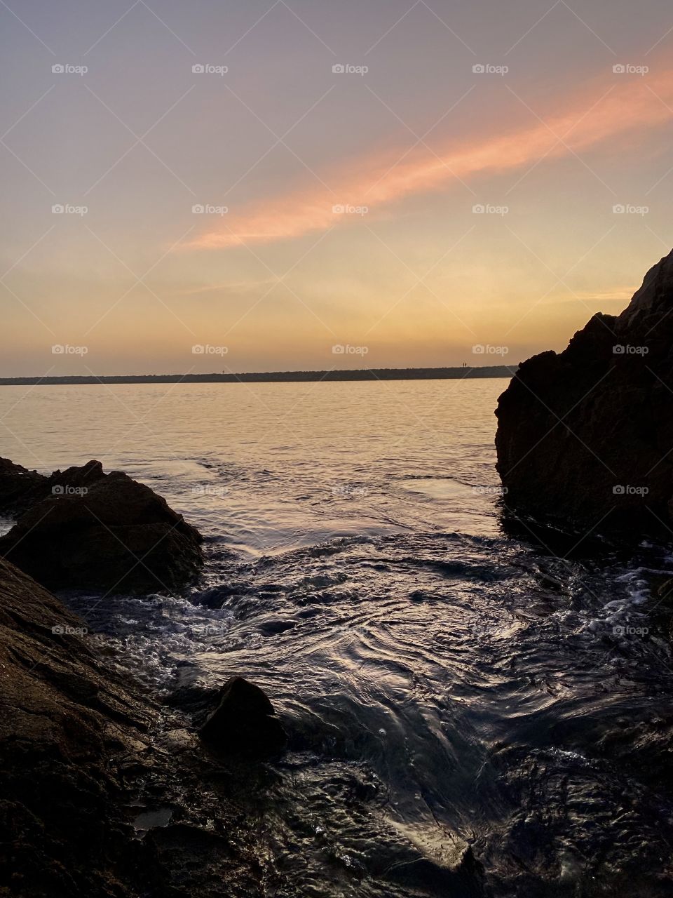 Sunset at Pirates Cove Beach in Corona del Mar with rocks in front of it 