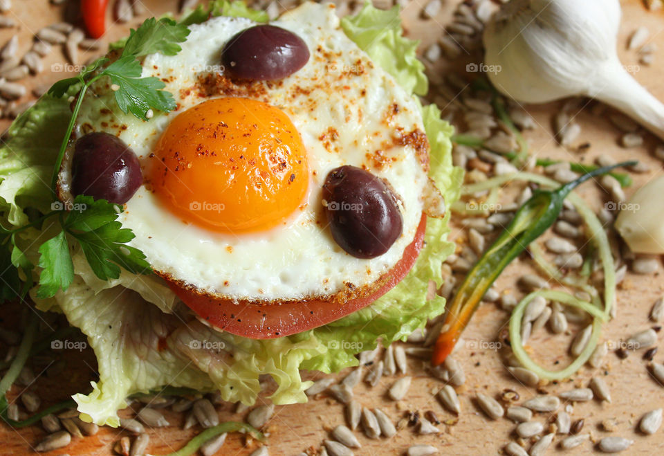 Tasty burger with fried egg, olives, lettuce, seeds, garlic, chili pepper