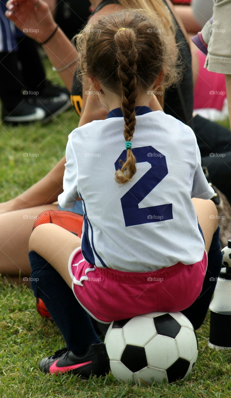 Little girl sitting on soccer ball during break at game