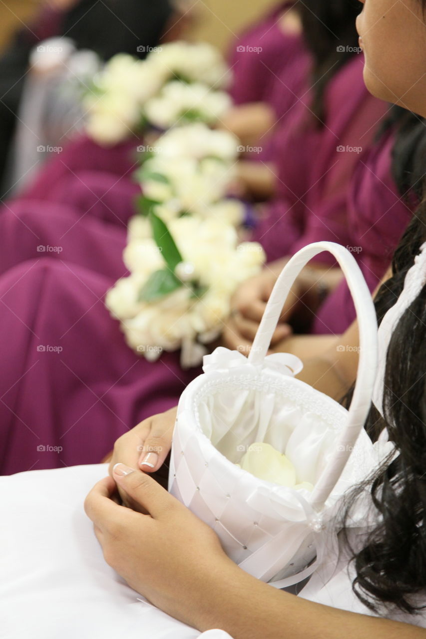 A flower girls basket rest in her lap as she listens at the wedding ceremony with the rest of the bridal party.