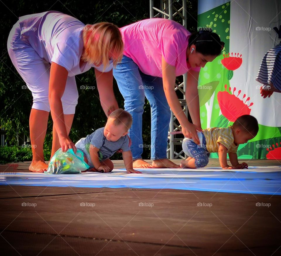 Small children.  Competition who is faster.  There are two mothers with their babies on the stage.  Moms prepare babies for the start